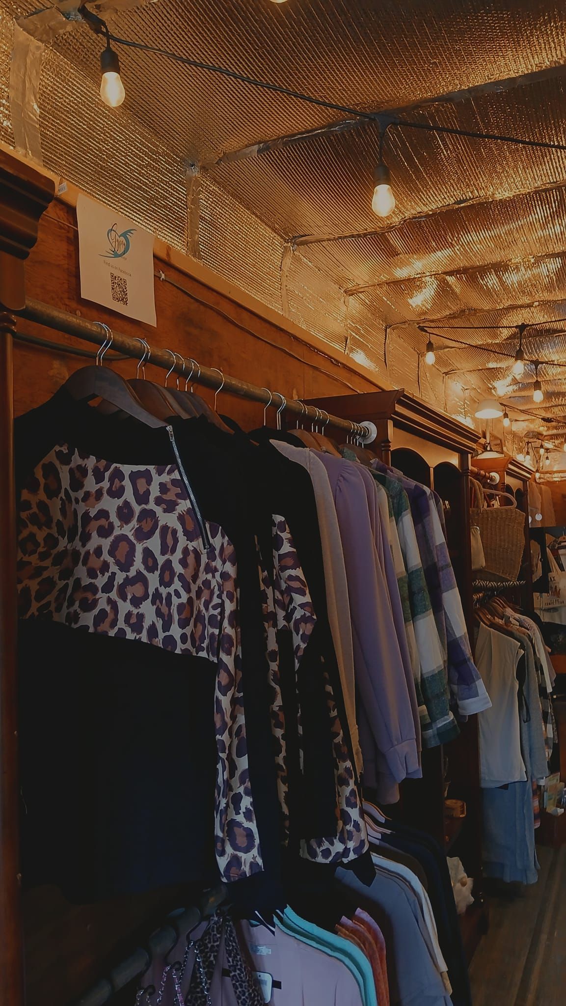 Clothing racks filled with shirts and pants in a rustic-style store with warm string lights hanging from the ceiling.