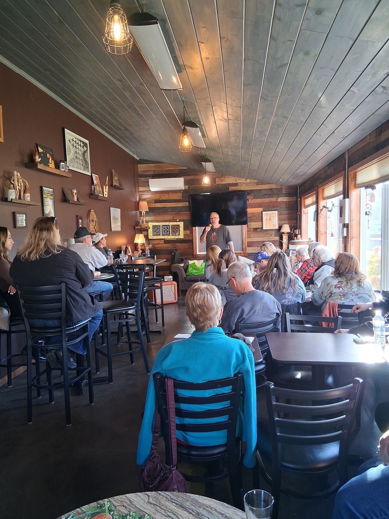 Dimly lit restaurant interior with dark wooden walls, multiple round tables, and black chairs.