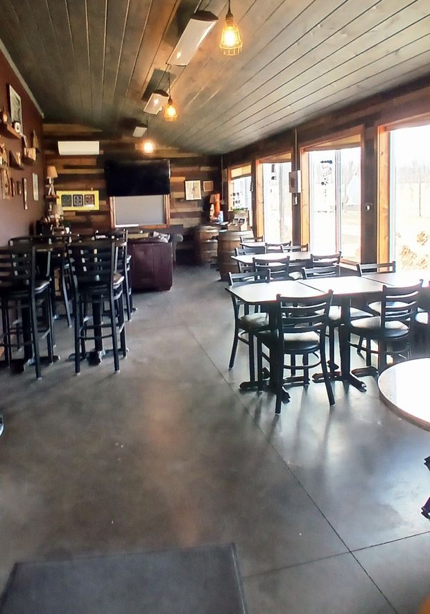 A dimly lit, wood-paneled room with small round tables and black chairs, illuminated by hanging light fixtures.