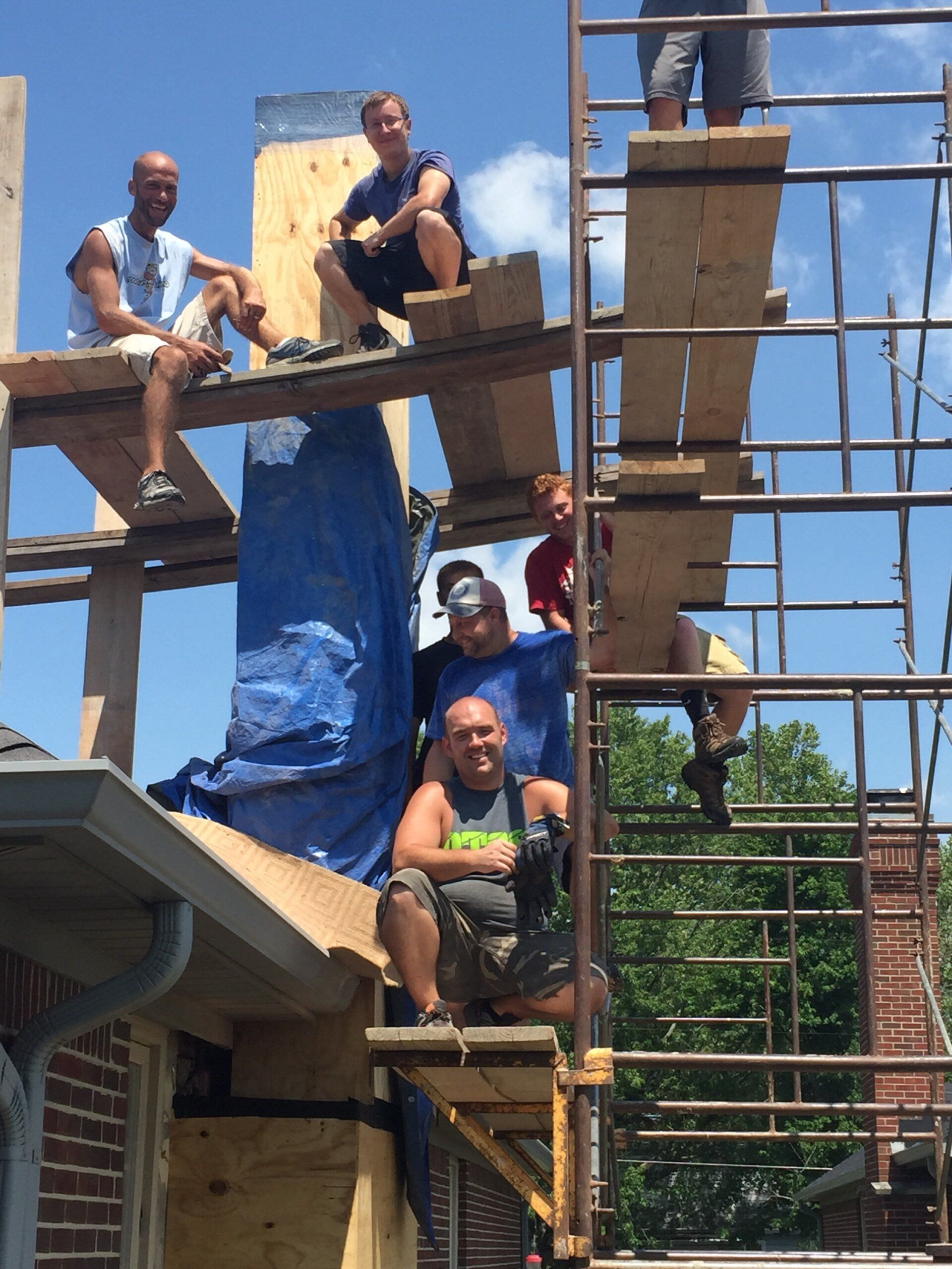 A group of men are sitting on scaffolding on top of a building