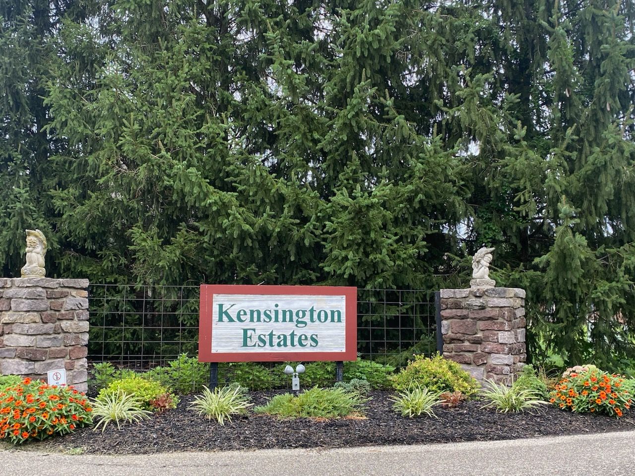 A sign for kensington estates is surrounded by trees and flowers