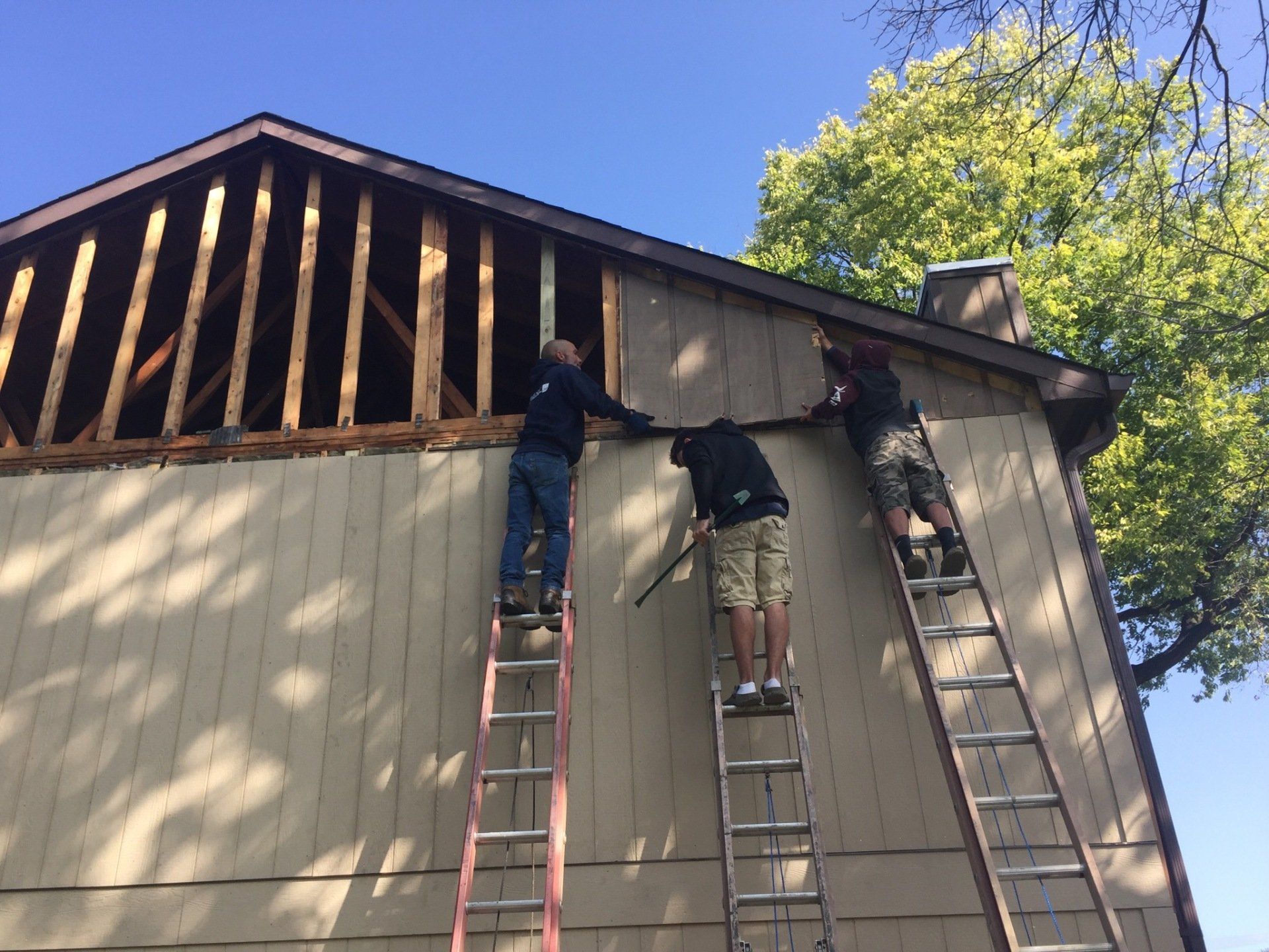 Two men on ladders are working on the side of a house