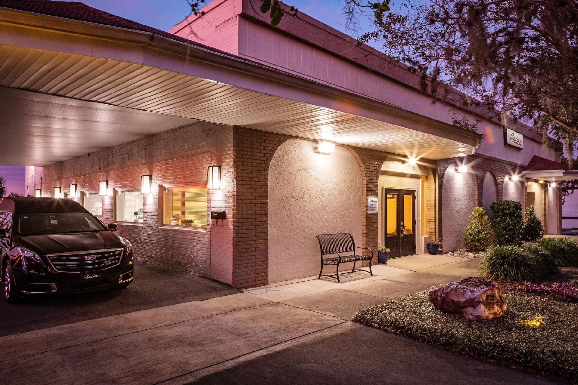 Exterior of a funeral home with a hearse parked under a covered entrance.