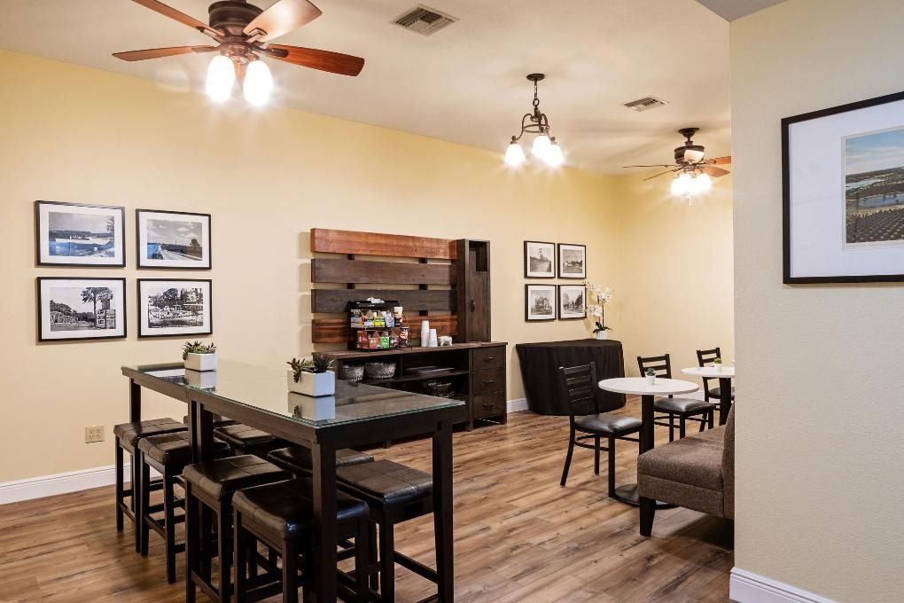 A cafe with tables, chairs, coffee station, and framed pictures on light yellow walls; wood floor.