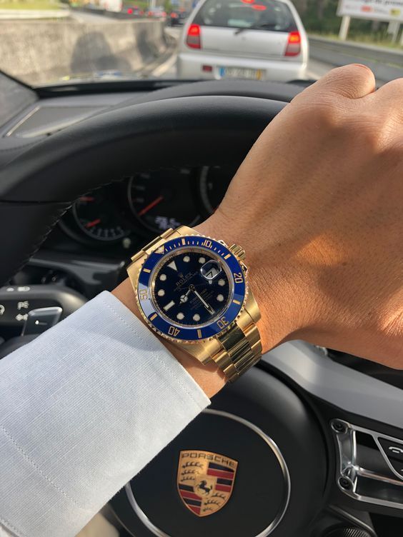 A man wearing a gold watch is driving a porsche