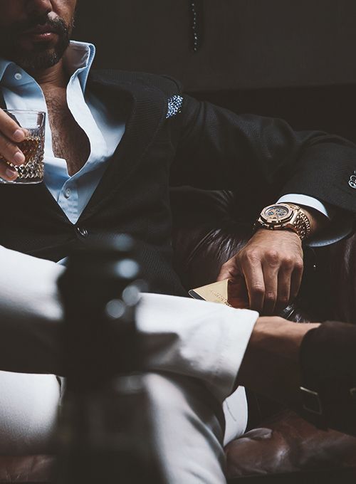 A man in a suit is sitting on a couch holding a glass of whiskey