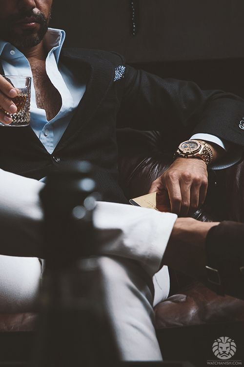 A man in a suit is sitting on a couch holding a glass of whiskey