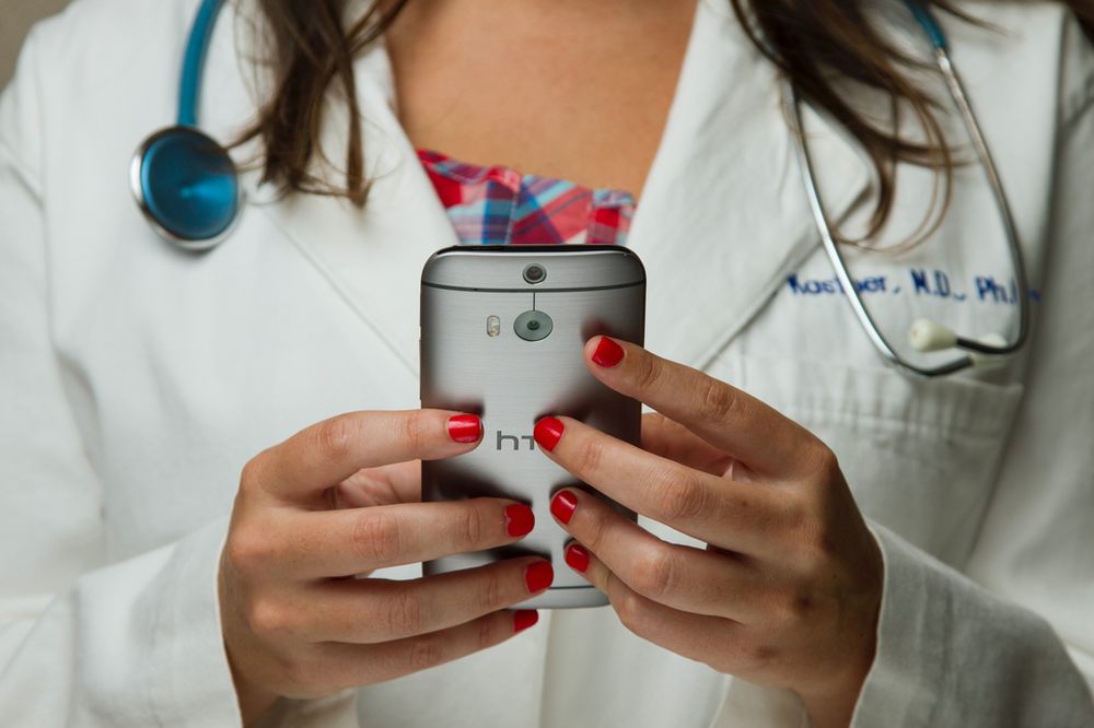 A doctor with a stethoscope around her neck is holding an htc phone