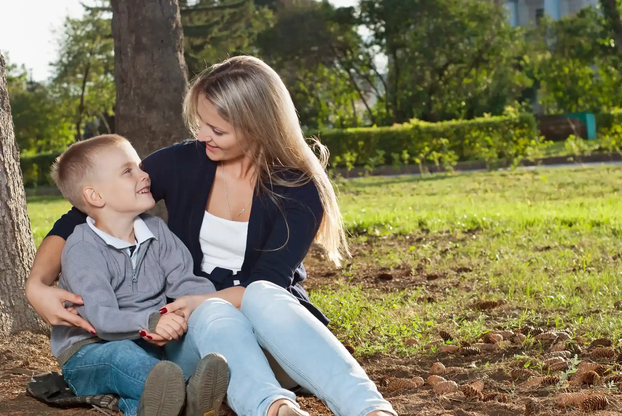 Woman and child sit in a park, smiling at each other.