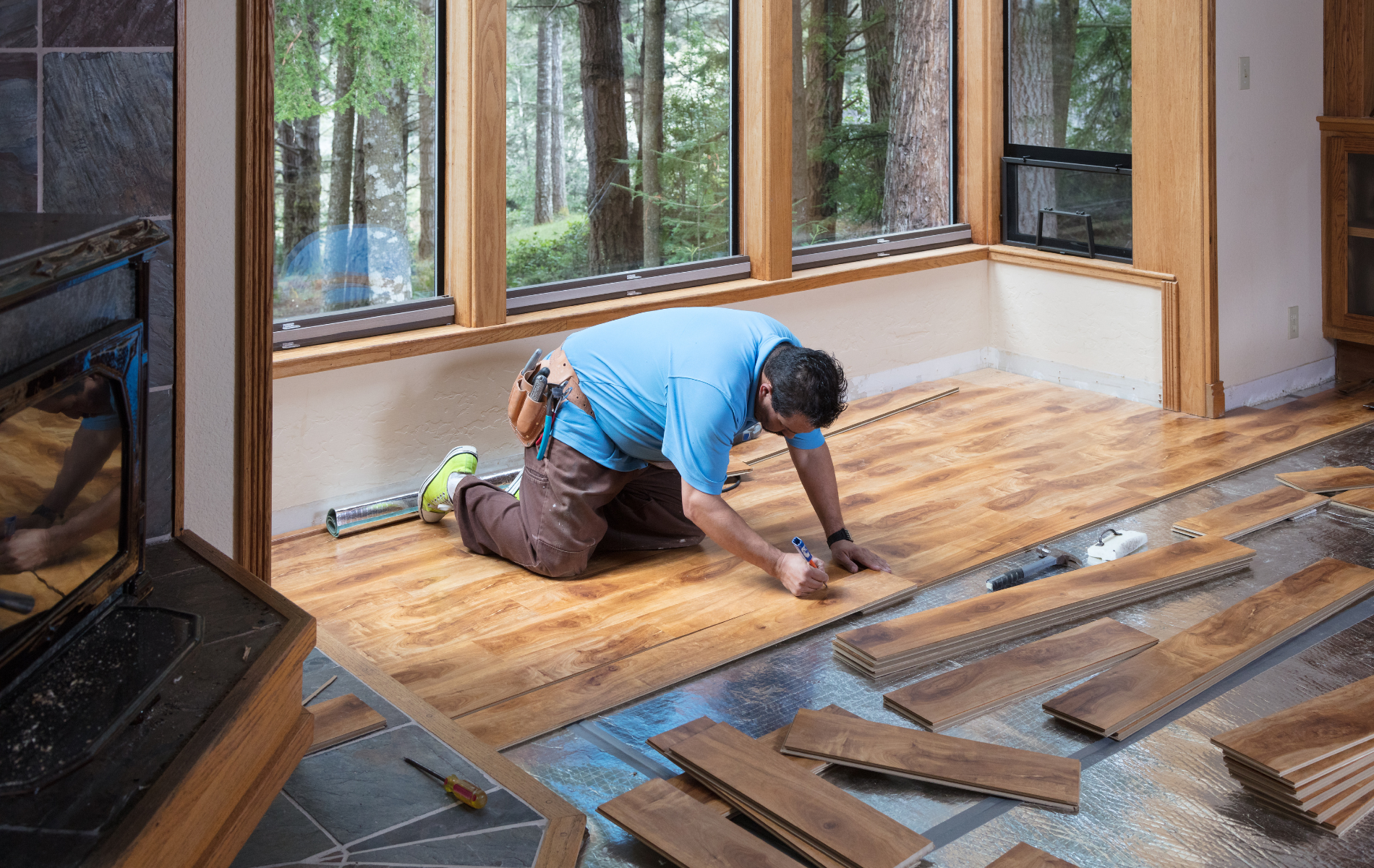 A man is installing hardwood flooring in a living room.