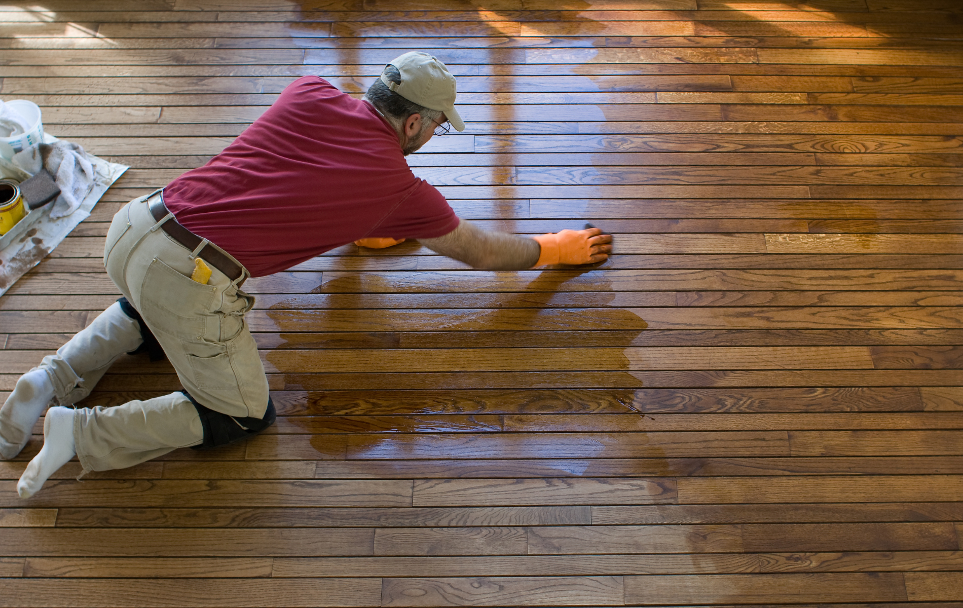 A man is kneeling on the floor polishing a wooden floor.