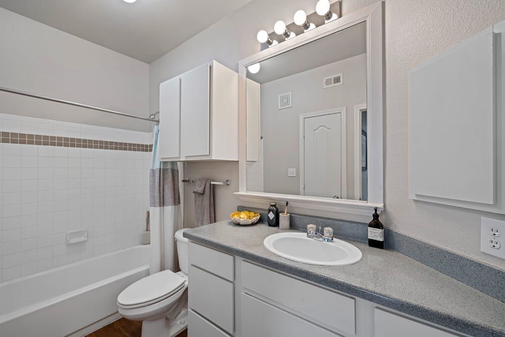 a bathroom with a sink, toilet, tub, and mirror at Marquis Parkside in Austin, TX.