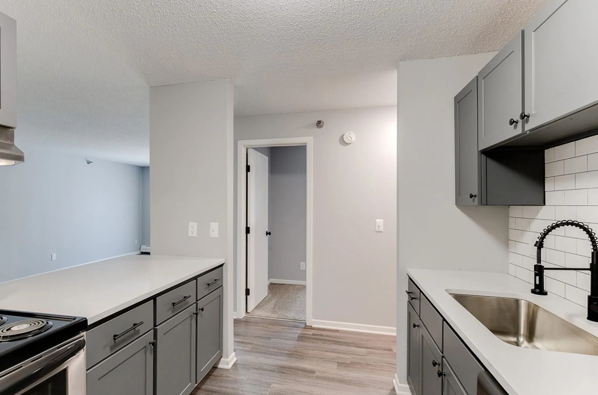 Gray kitchen with cabinets, white countertops, subway tile backsplash, stainless steel appliances, and a hallway.