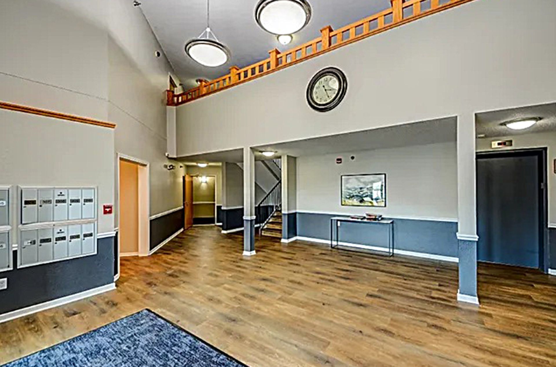 Lobby with wood floors, mailboxes, and a dark blue rug. A clock and artwork hang on the walls.