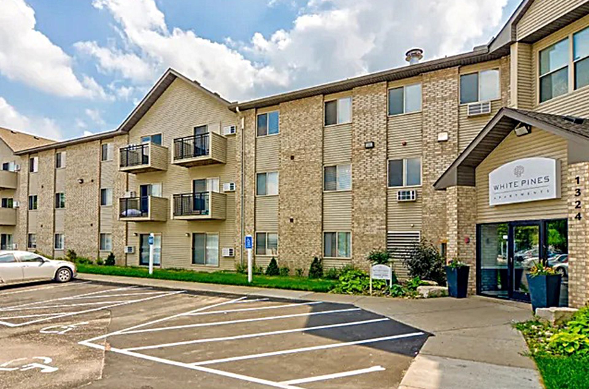 Apartment building exterior with parking, entry, balconies, and blue sky.