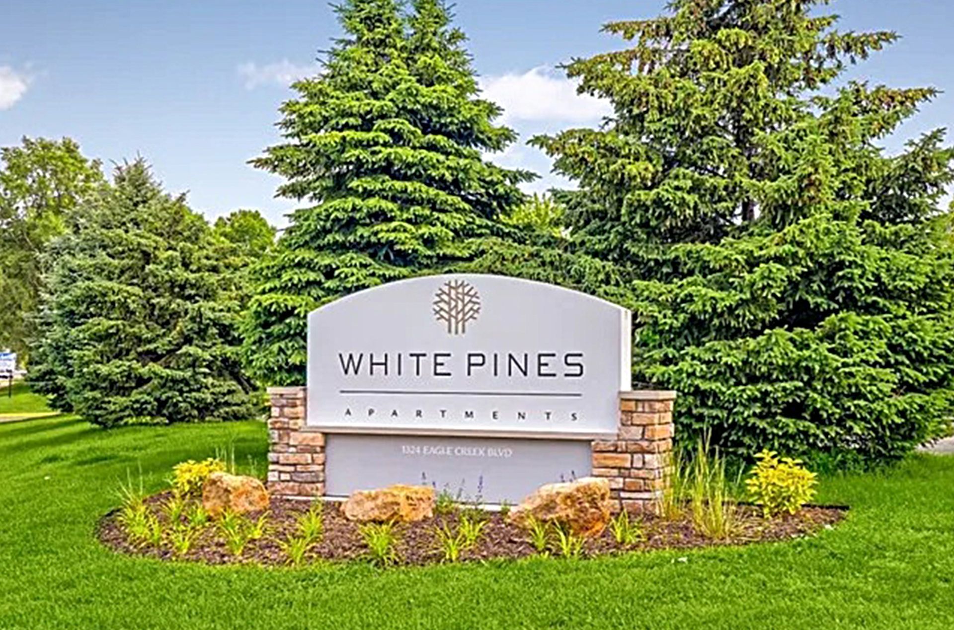 White Pines Apartments sign with landscaping, trees, and grass.