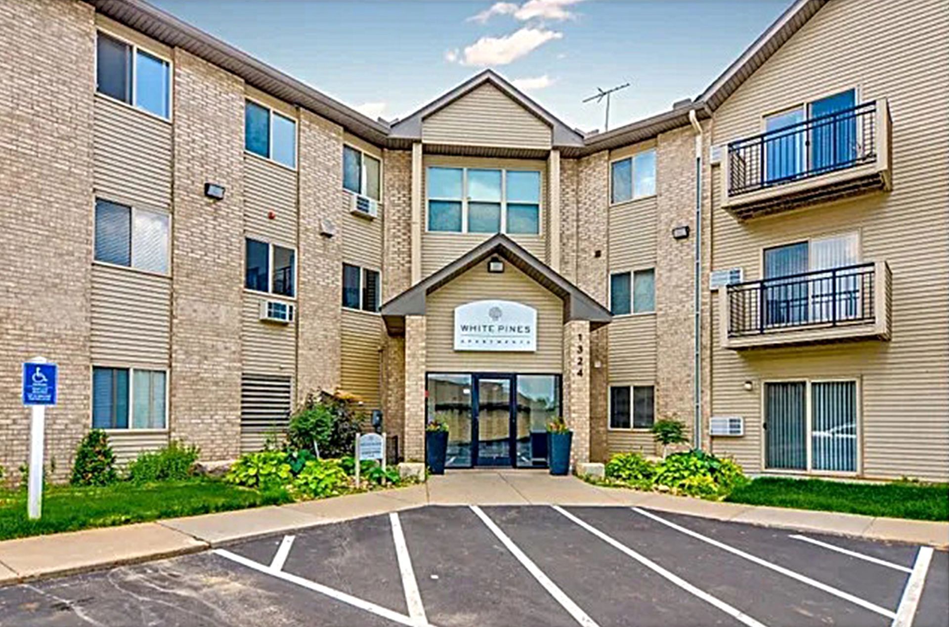 Apartment building exterior with a wheelchair-accessible parking sign; beige siding, three stories.