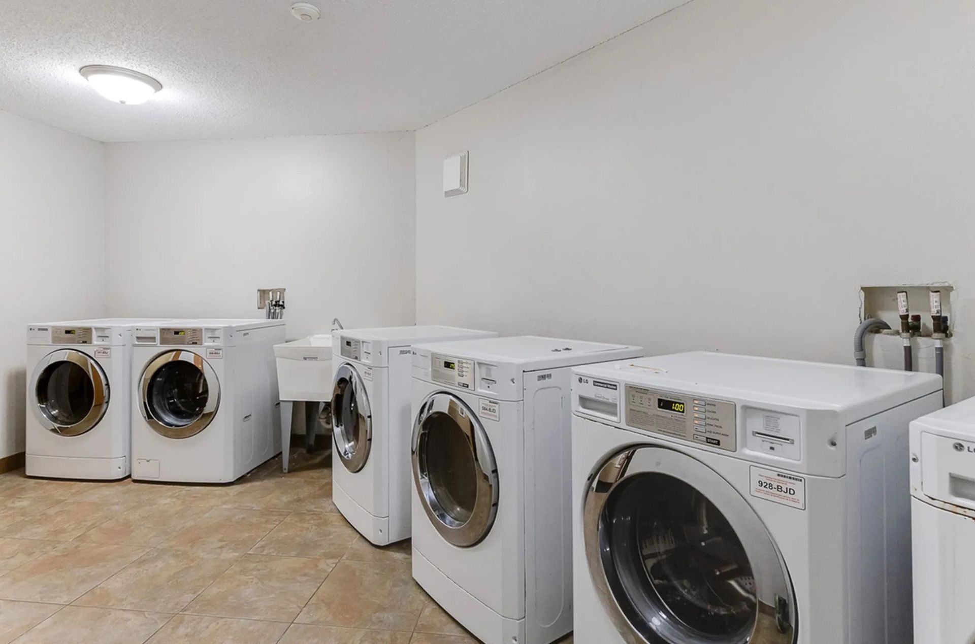 Laundry room with several white washing machines and a utility sink.