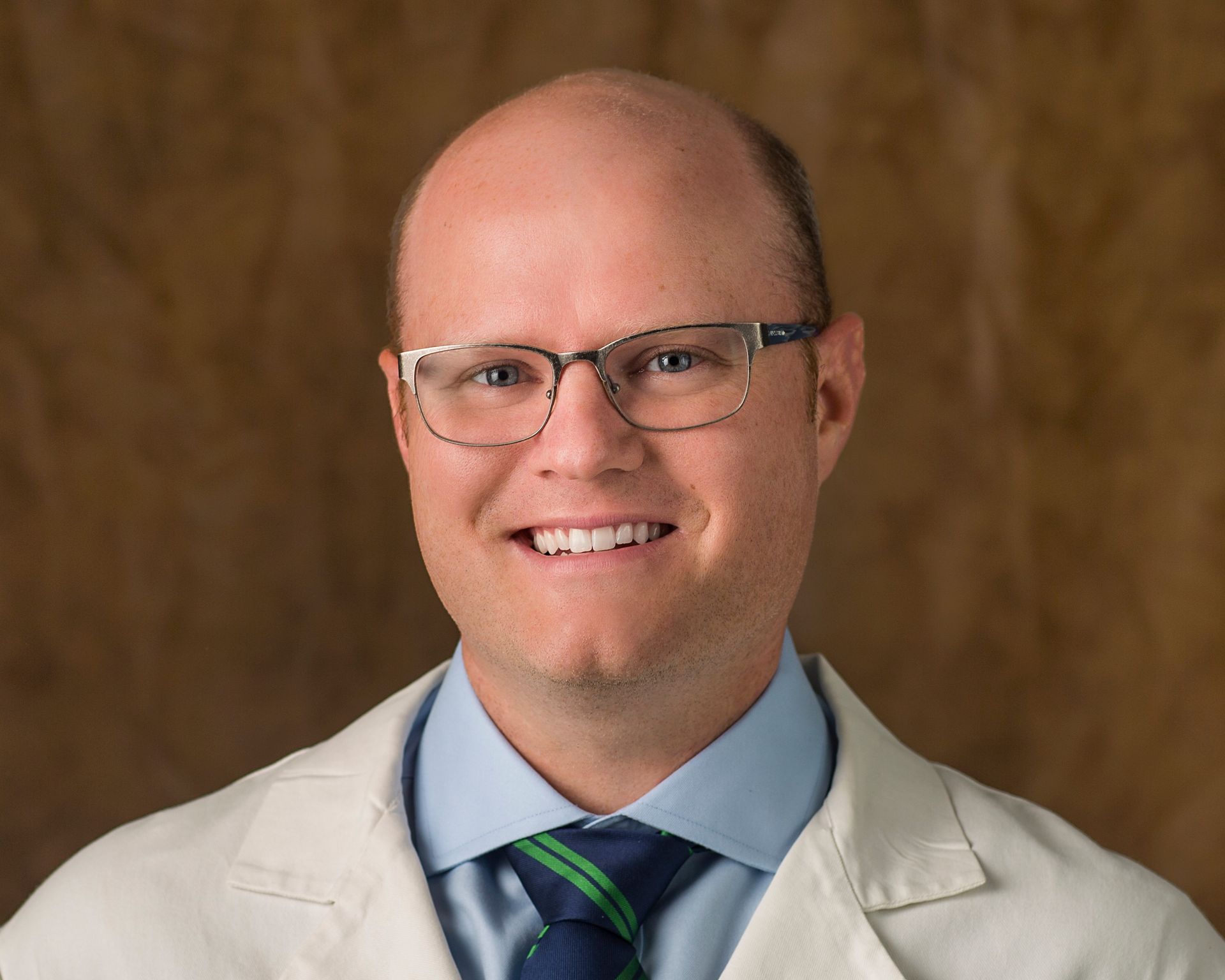 A bald man wearing glasses and a white coat is smiling for the camera.