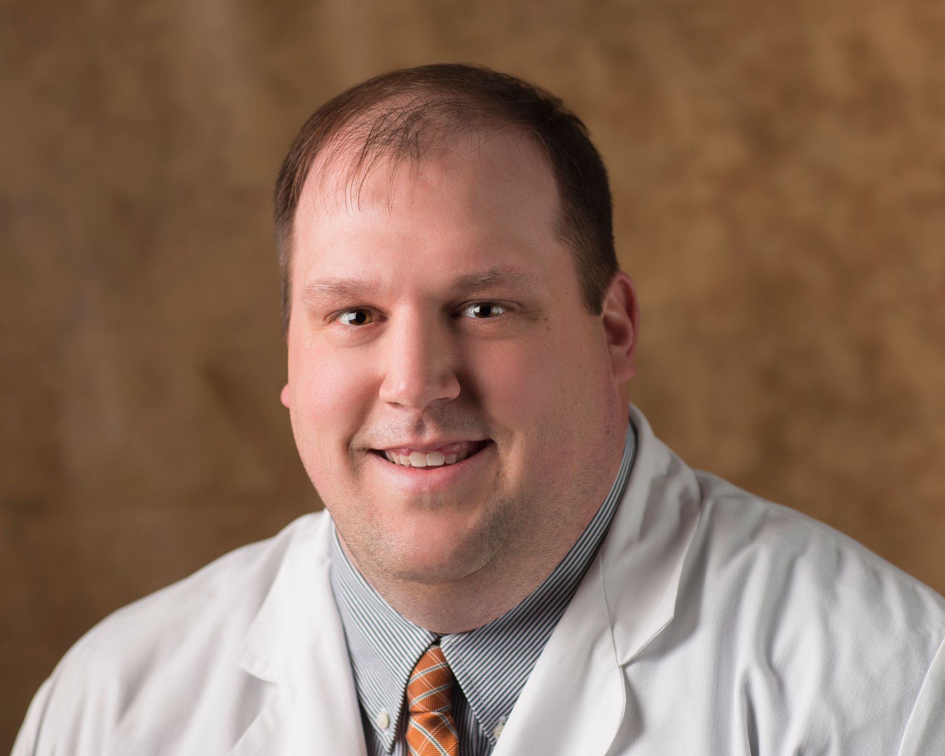 A man in a white coat and tie is smiling for the camera.