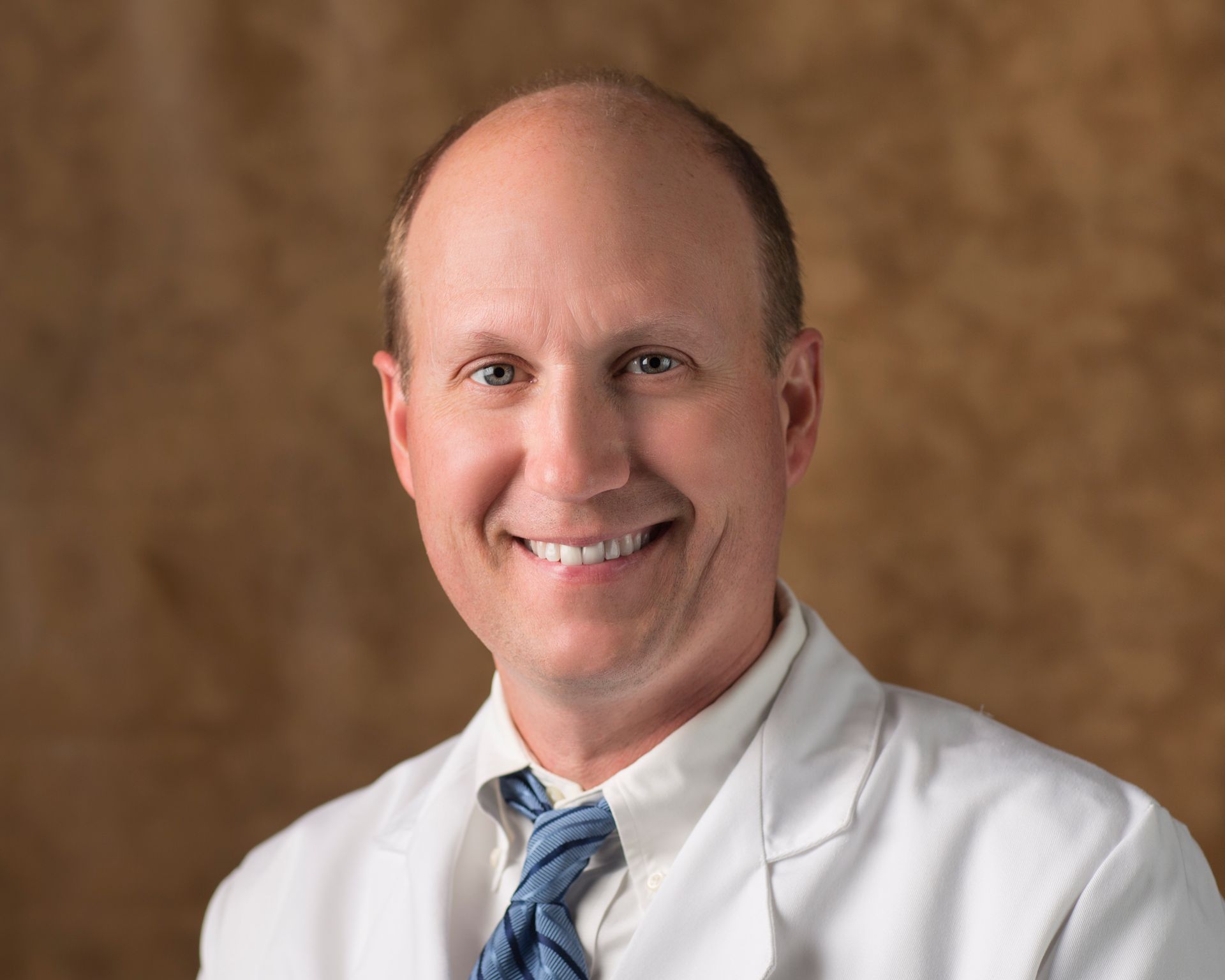 A man in a white coat and tie is smiling for the camera.