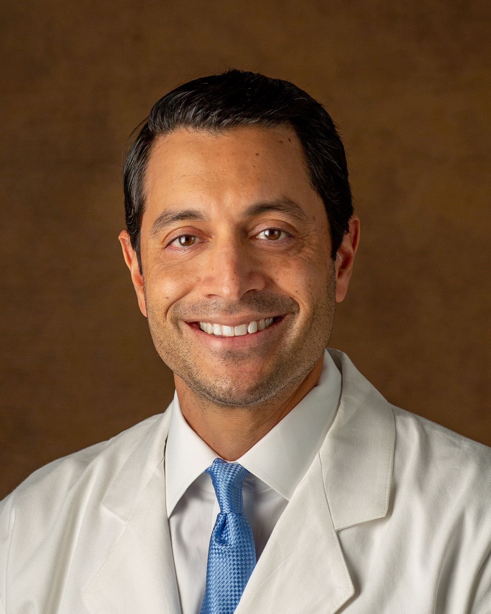 A man in a white coat and blue tie is smiling for the camera.