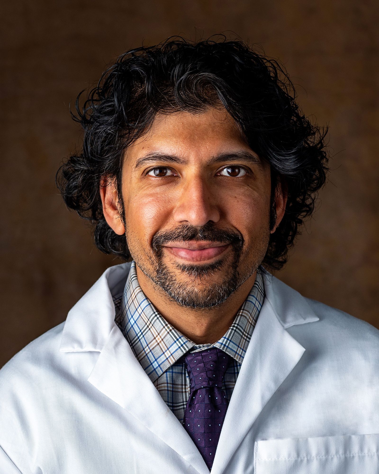 A man with a beard is wearing a white coat and tie.