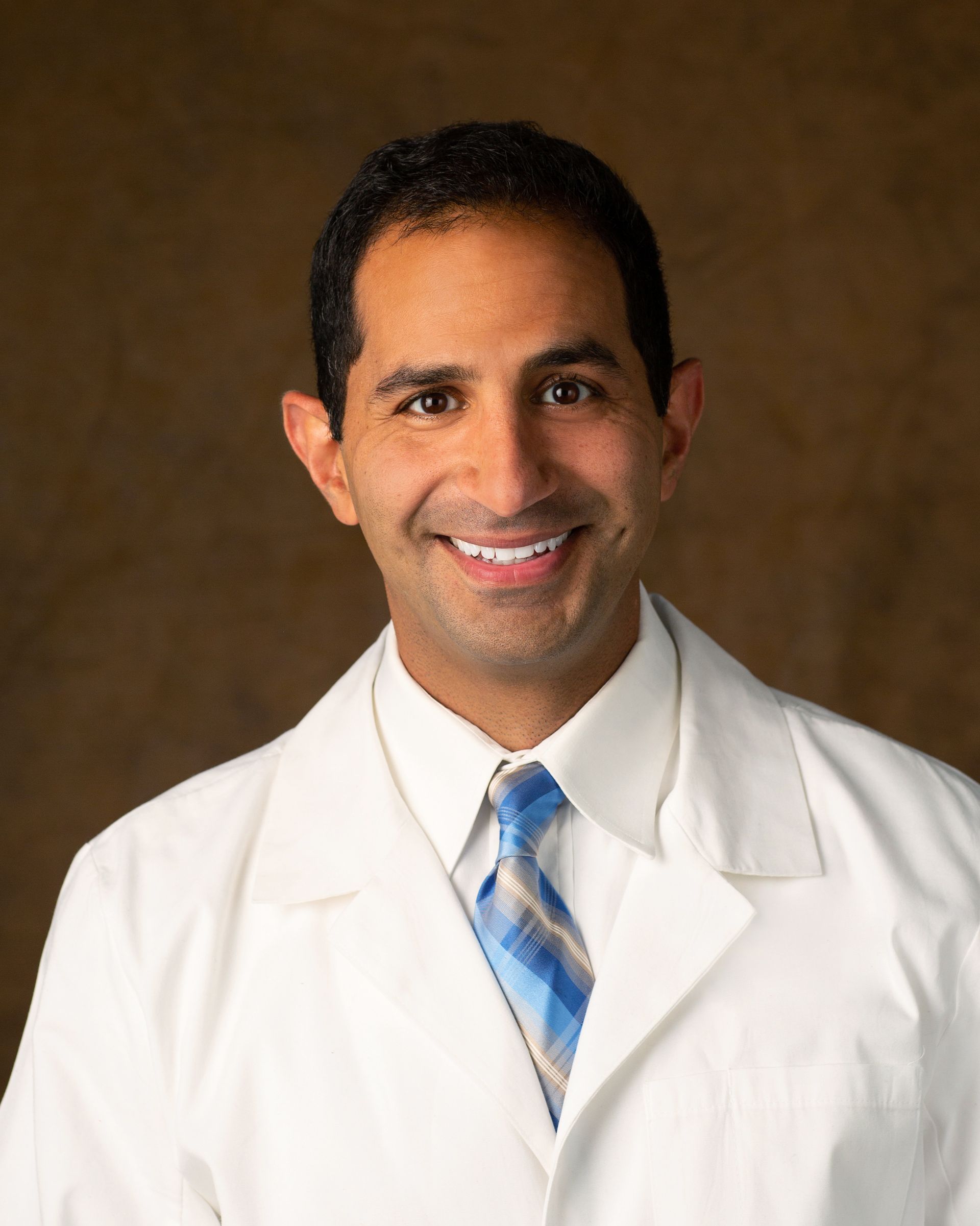 A man in a white coat and blue tie smiles for the camera