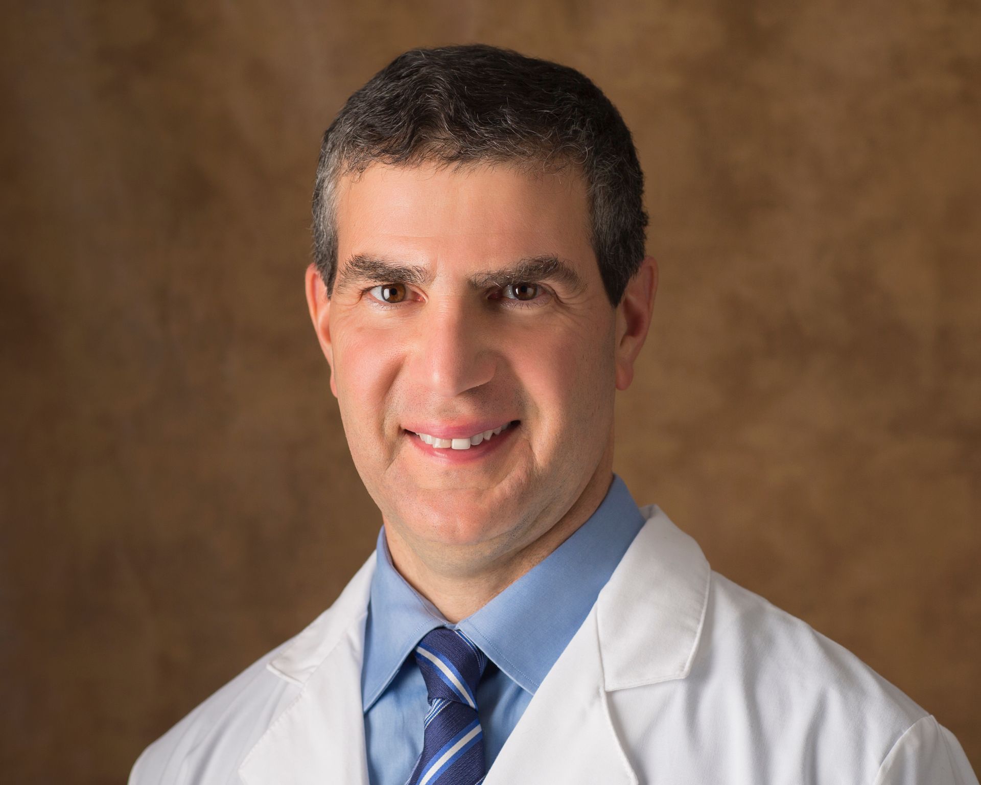 A man in a white coat and tie is smiling for the camera