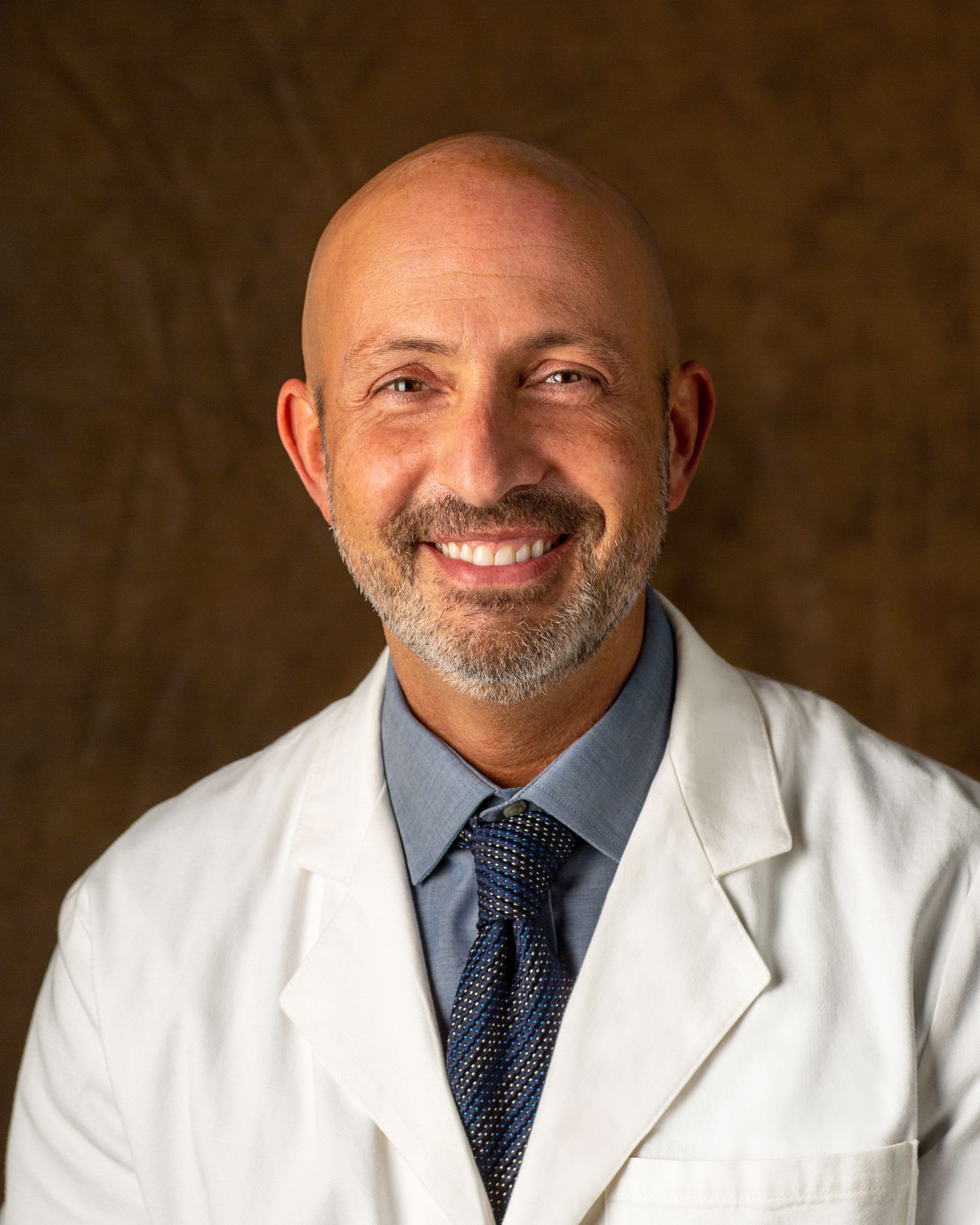 A bald man with a beard is wearing a white coat and tie.