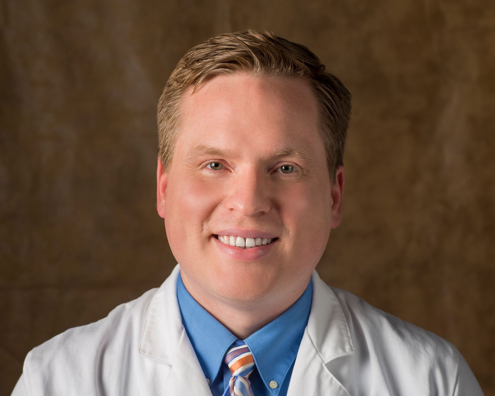 A man in a white coat and tie smiles for the camera