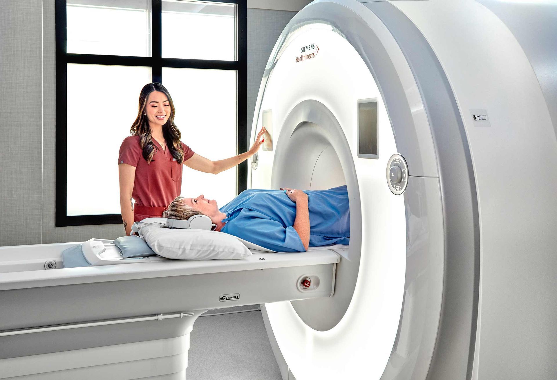 A woman is standing next to a patient laying in a mri machine.