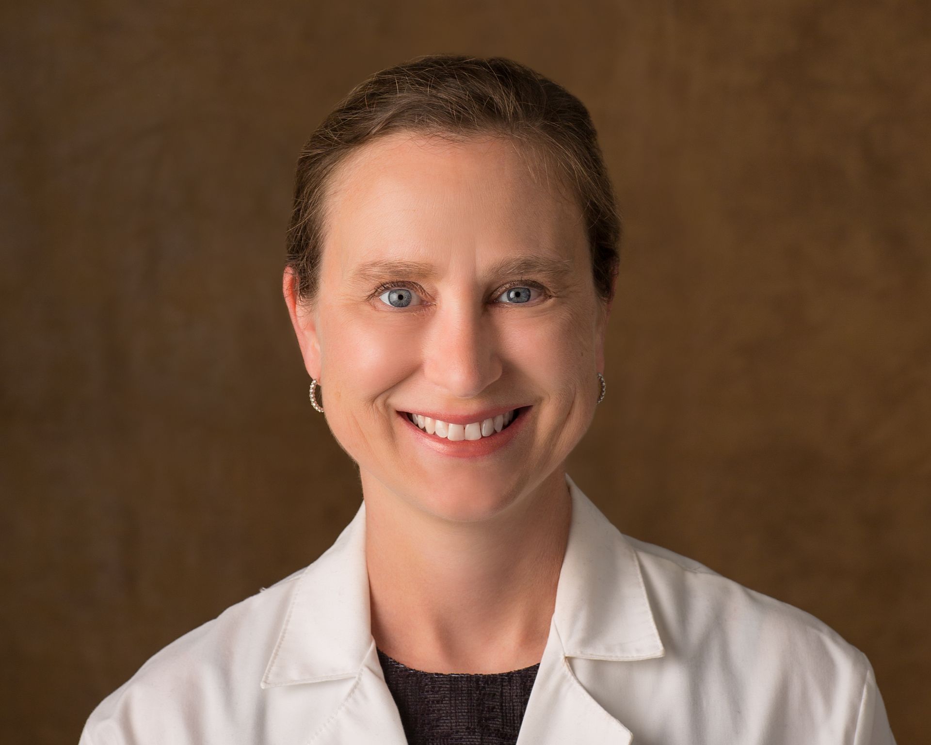 A woman in a white lab coat is smiling for the camera.