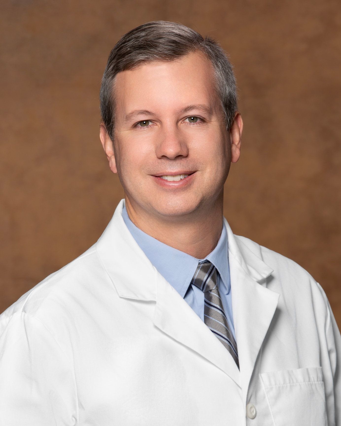 A man in a white coat and tie is smiling for the camera.