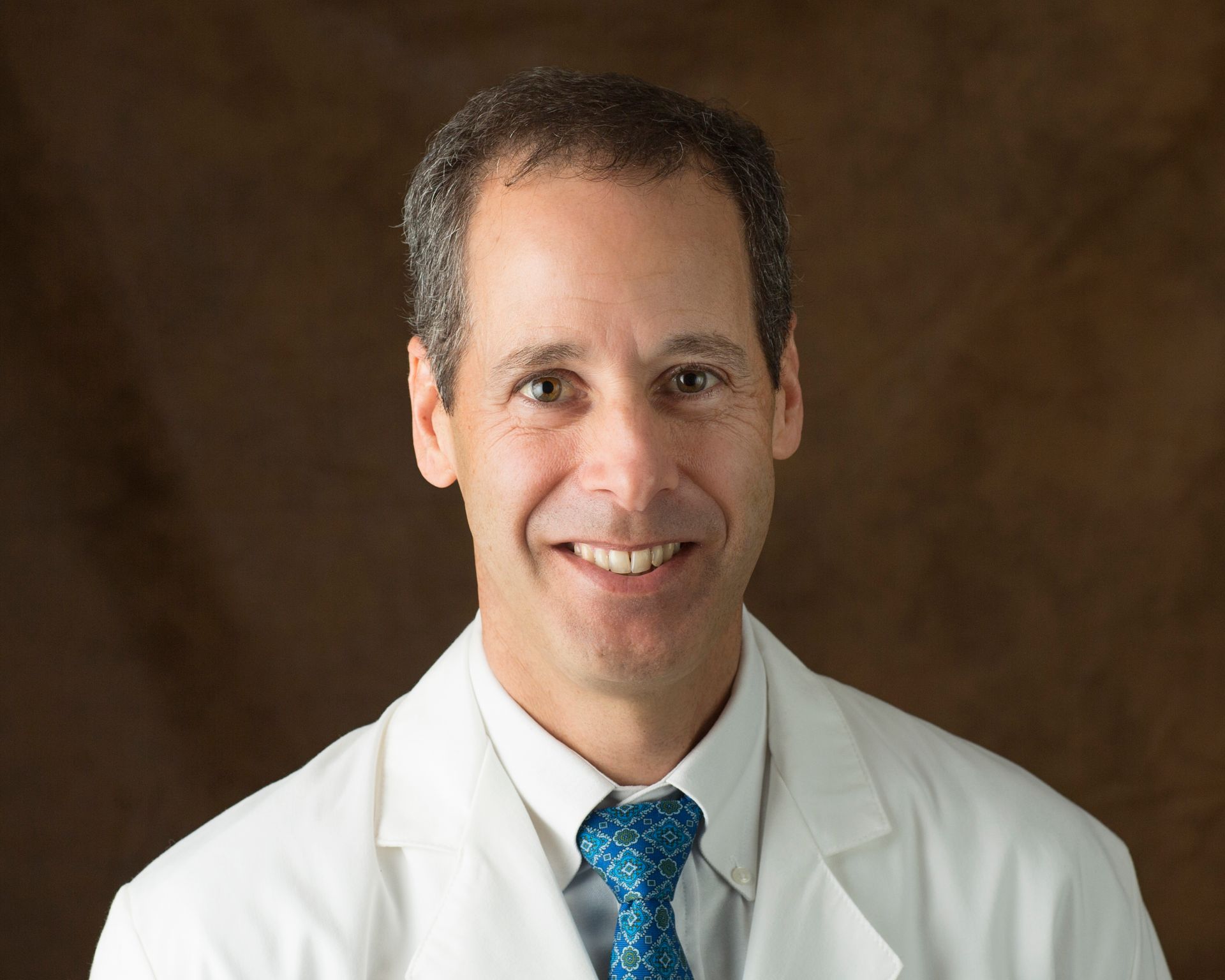 A man in a white coat and tie is smiling for the camera.