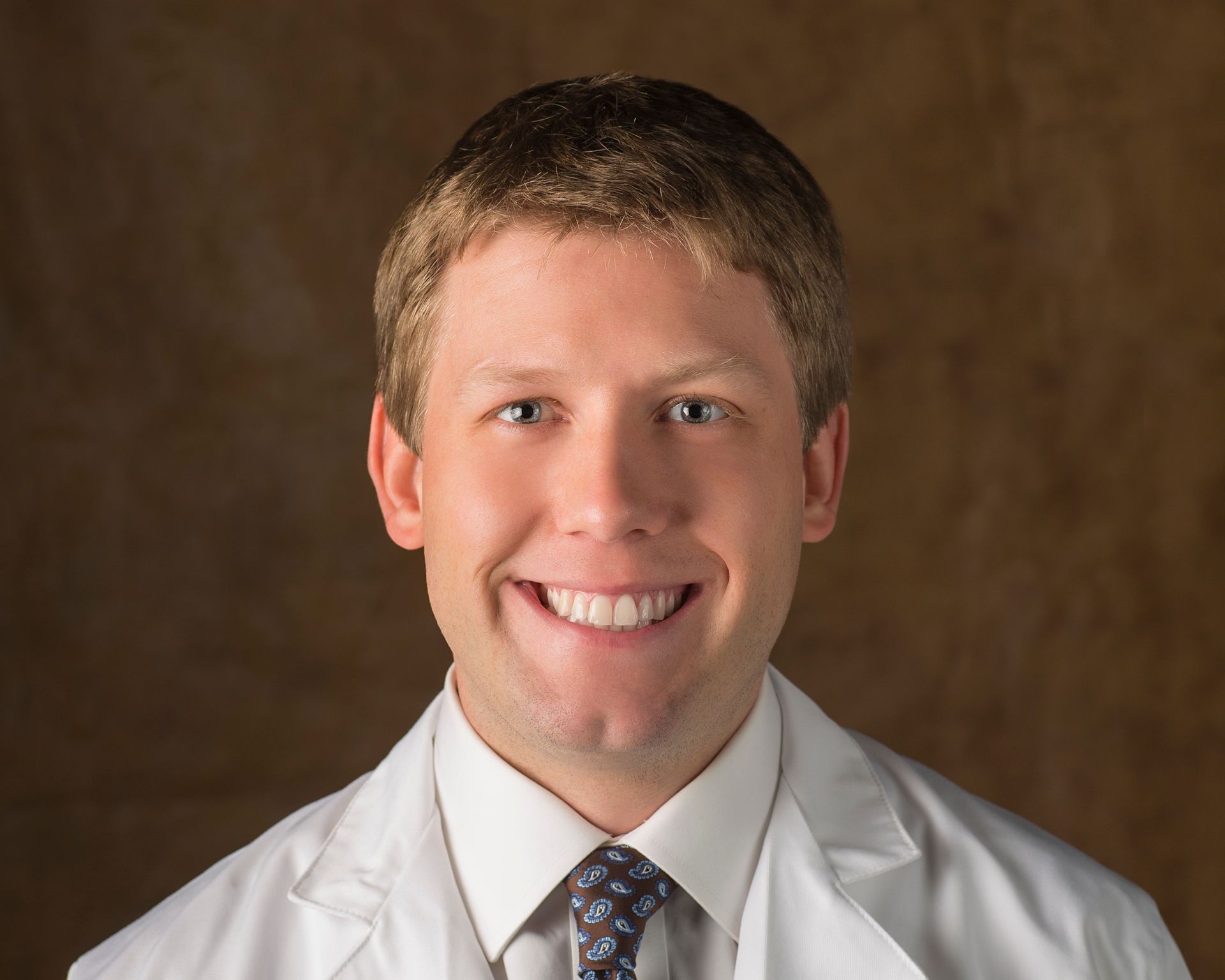 A man in a white coat and tie is smiling for the camera.