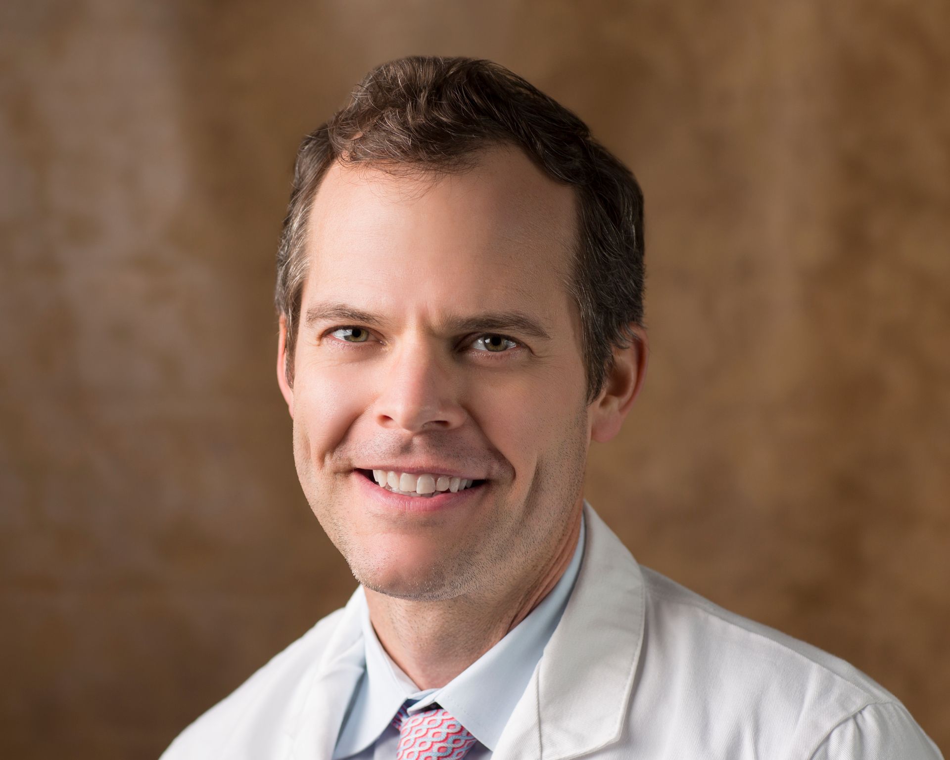 A man in a white coat and tie is smiling for the camera.