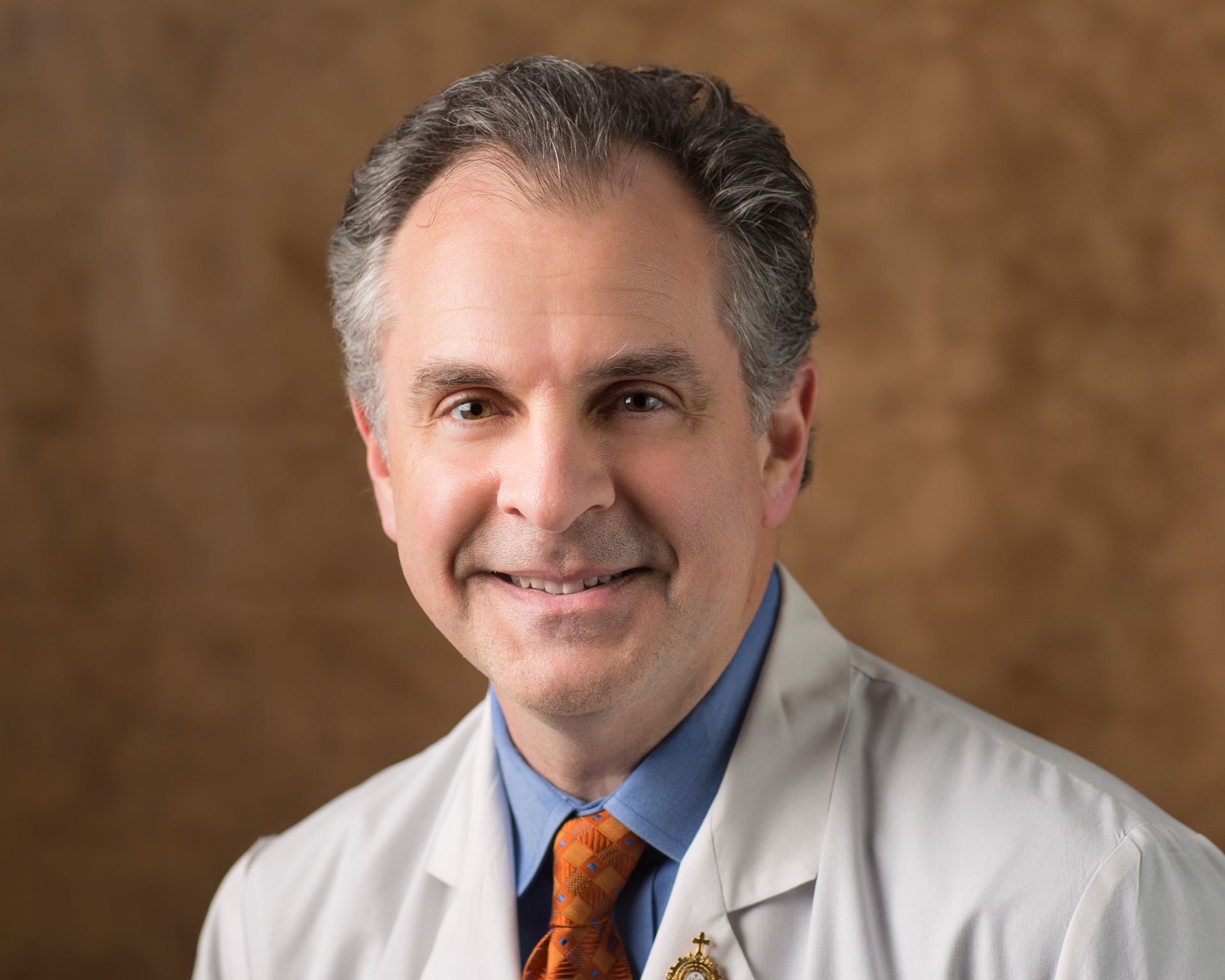 A man in a white coat and tie is smiling for the camera.