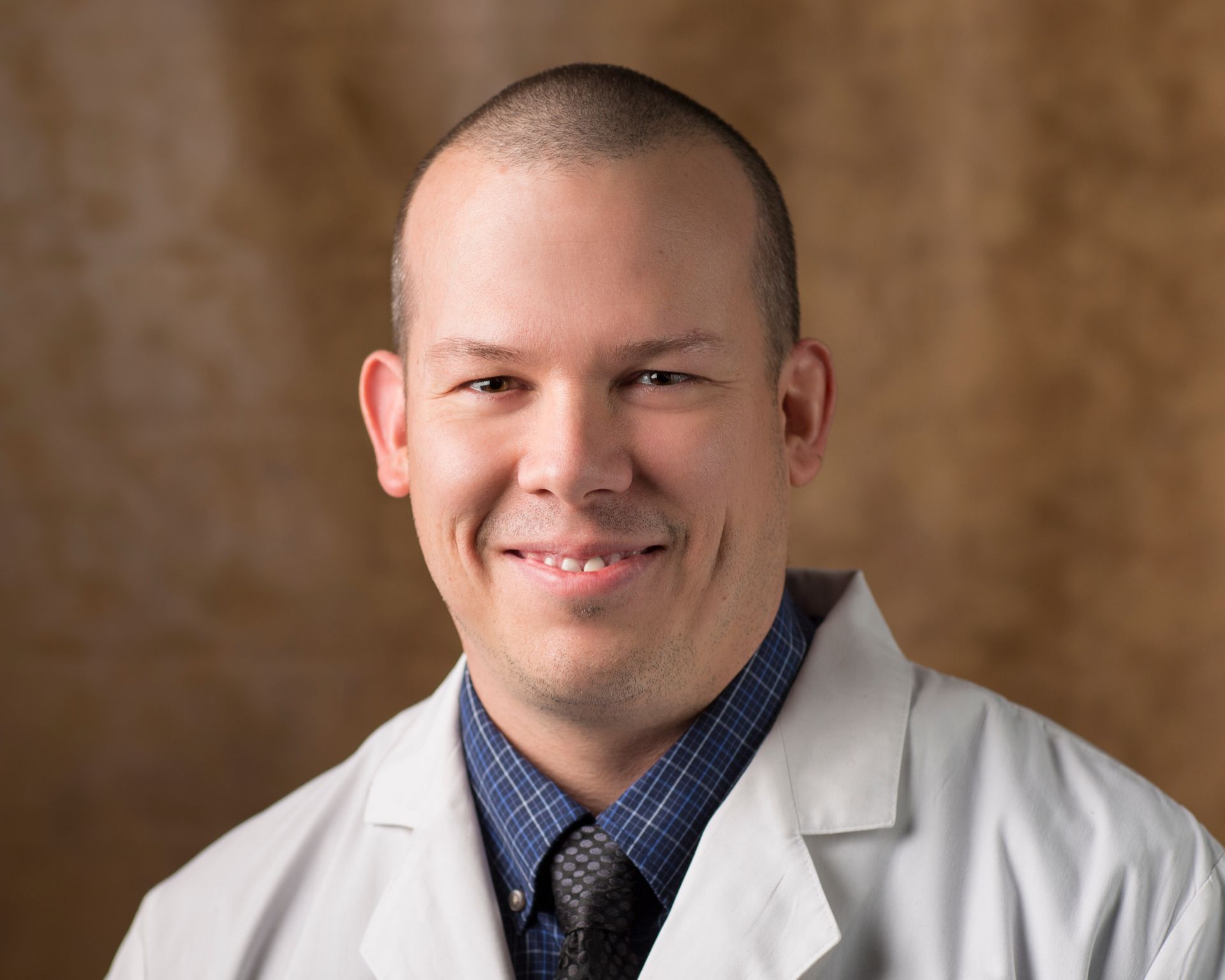 A man in a white coat and tie is smiling for the camera.