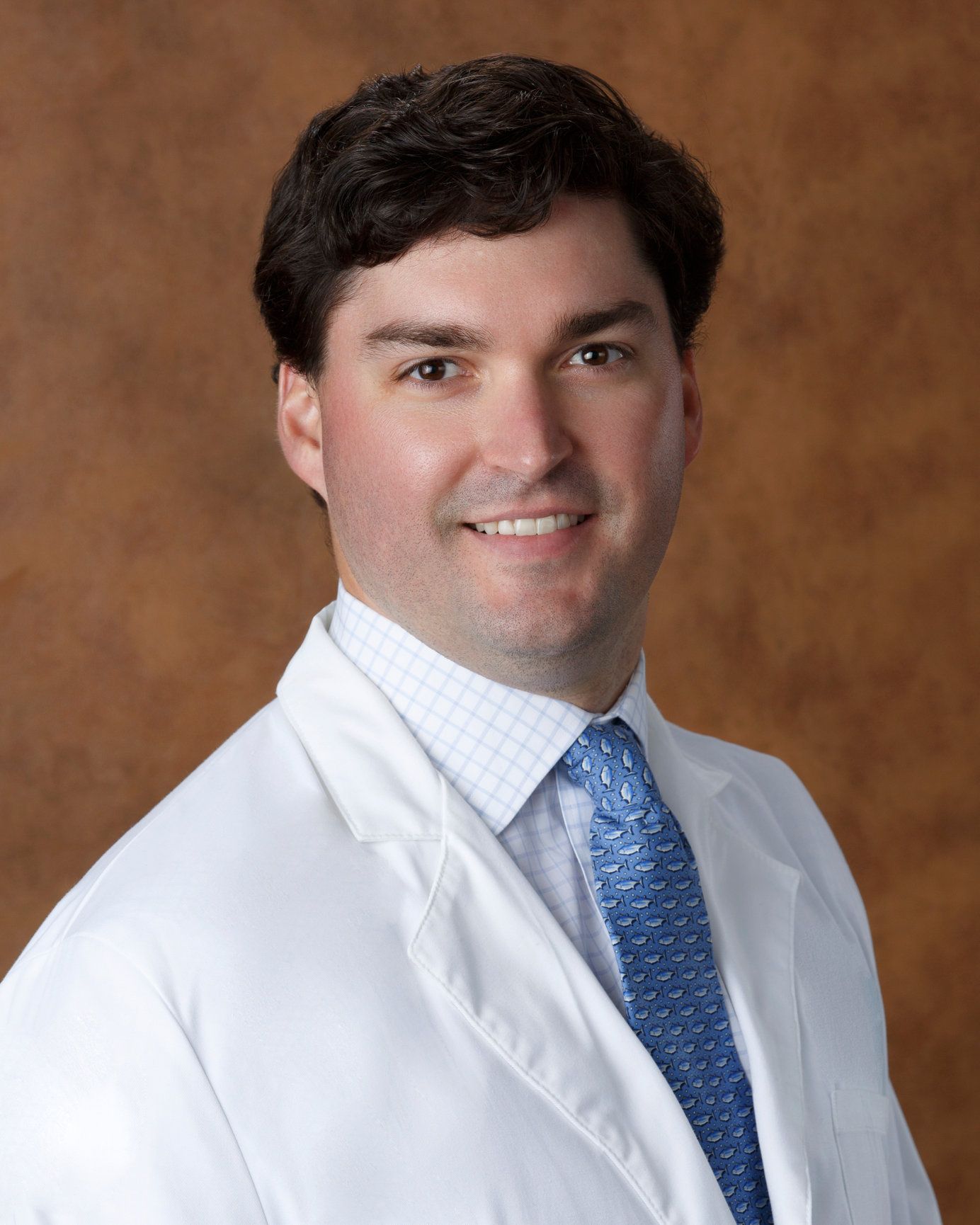 A man in a white coat and blue tie smiles for the camera
