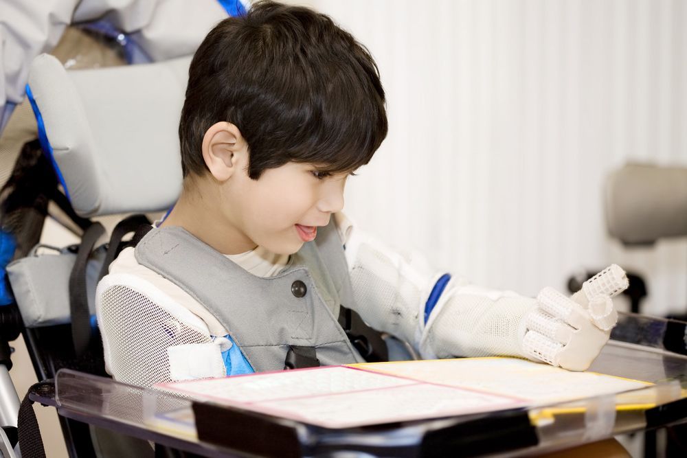A Young Boy in a Wheelchair is Writing on a Piece of Paper — Adaptive Care Pty Ltd In Tarneit, VIC