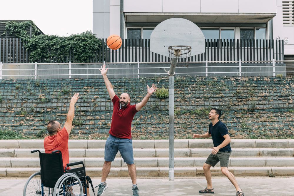 Joyful Disabled Man in Wheelchair Throwing the Ball to Basket with Friends — Adaptive Care Pty Ltd In Sunshine, VIC