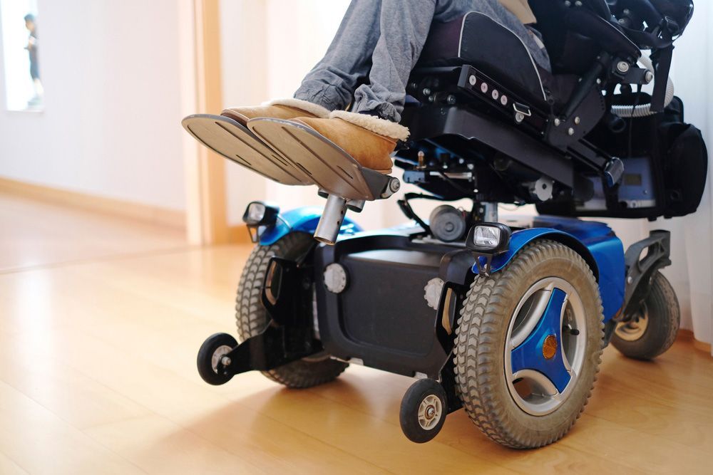 A Disabled Woman Sitting in a Blue Electric Wheelchair Indoors — Adaptive Care Pty Ltd In Tarneit, VIC