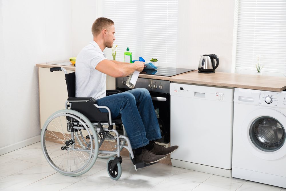 Young Handicapped Man On Wheelchair Cleaning Induction Stove— Adaptive Care Pty Ltd In Sunshine, VIC