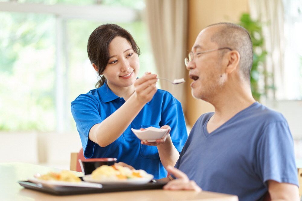 A Woman Assists an Elderly Man by Feeding Him With a Spoon — Adaptive Care Pty Ltd In Epping, VIC