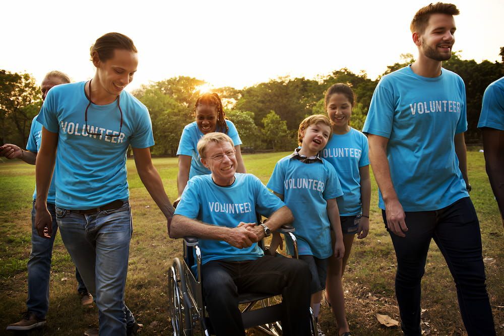 A Group Of Volunteers Are Walking With A Man In A Wheelchair — Adaptive Care Pty Ltd In Tarneit, VIC