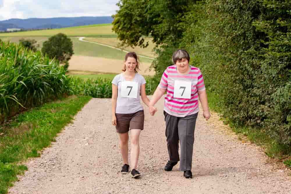 Two Women Are Walking Down A Dirt Road Holding Hands — Adaptive Care Pty Ltd In Tarneit, VIC
