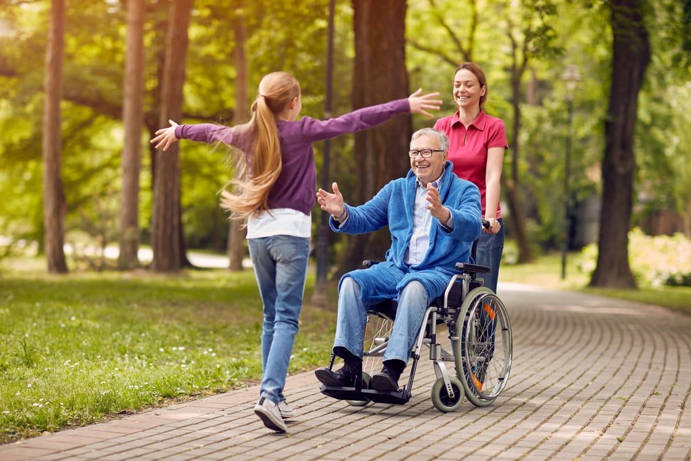 A Little Girl is Running Towards an Elderly Man in a Wheelchair — Adaptive Care Pty Ltd In Tarneit, VIC