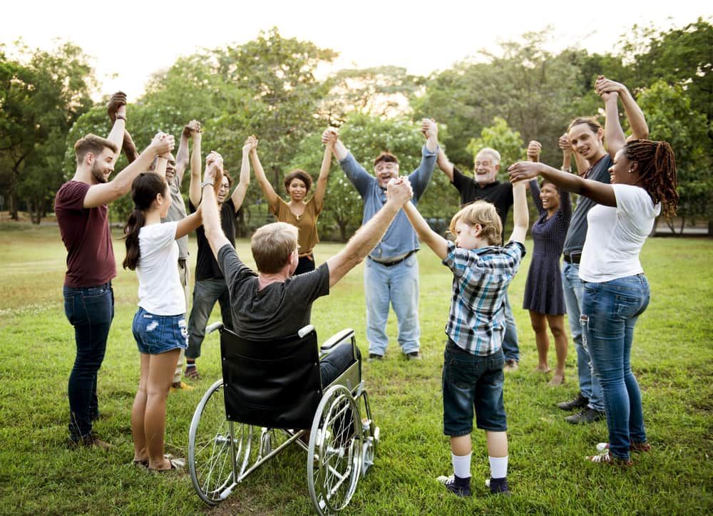 A Group Of People Are Holding Hands In A Circle With A Man In A Wheelchair — Adaptive Care Pty Ltd In Tarneit, VIC