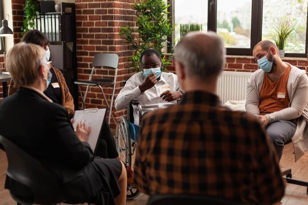 A Group Of People Wearing Face Masks Are Sitting In A Circle — Adaptive Care Pty Ltd In Tarneit, VIC